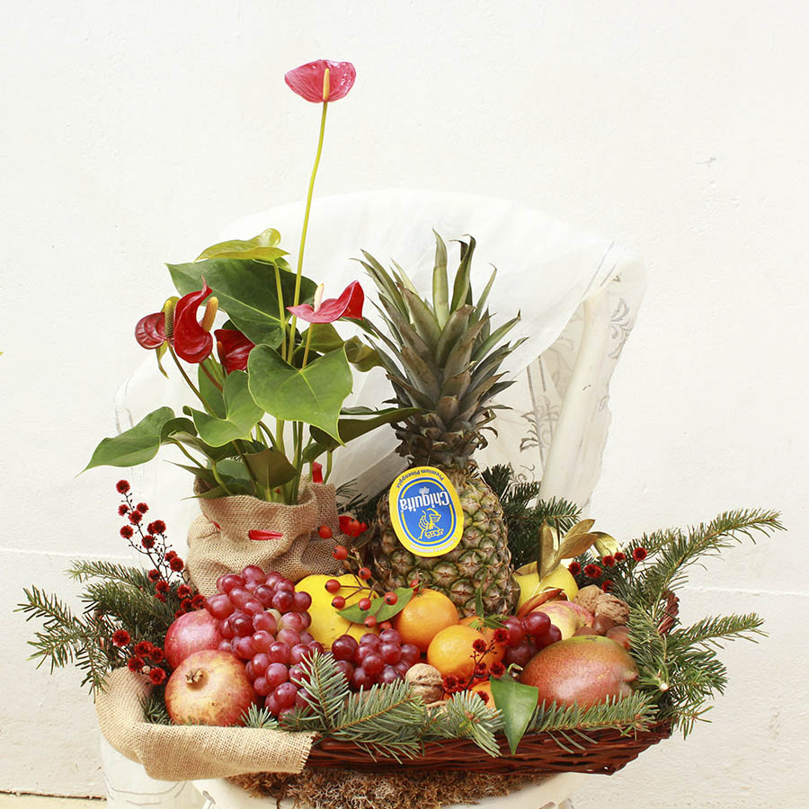 Gran cesta navideña con frutas variadas, planta y verdes navideños.